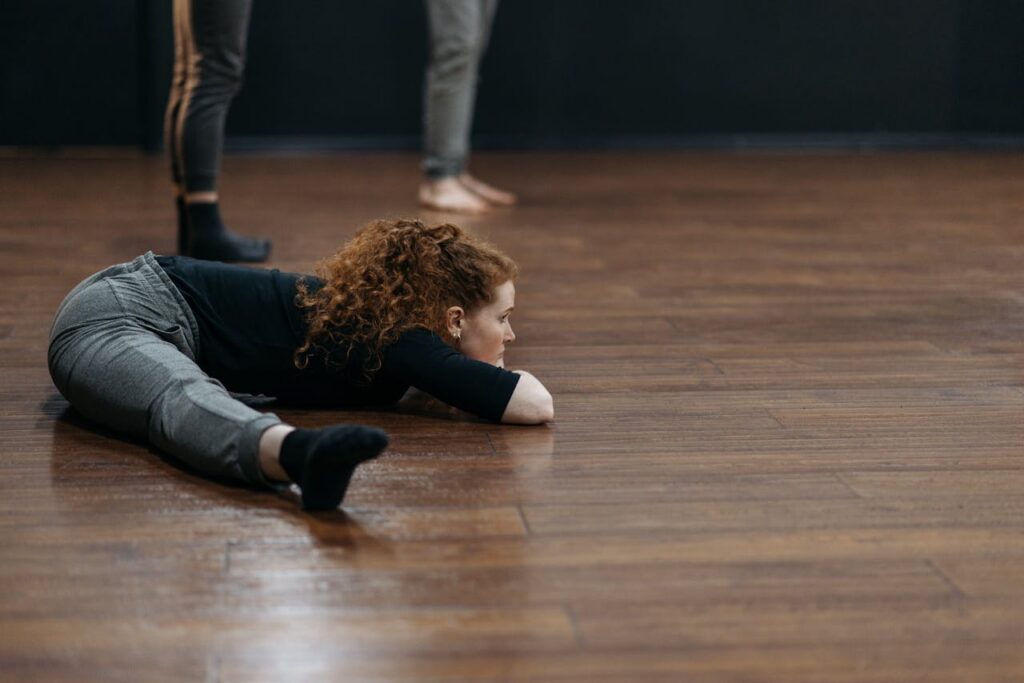 A contemporary dancer lying on a wooden floor in a dance studio.